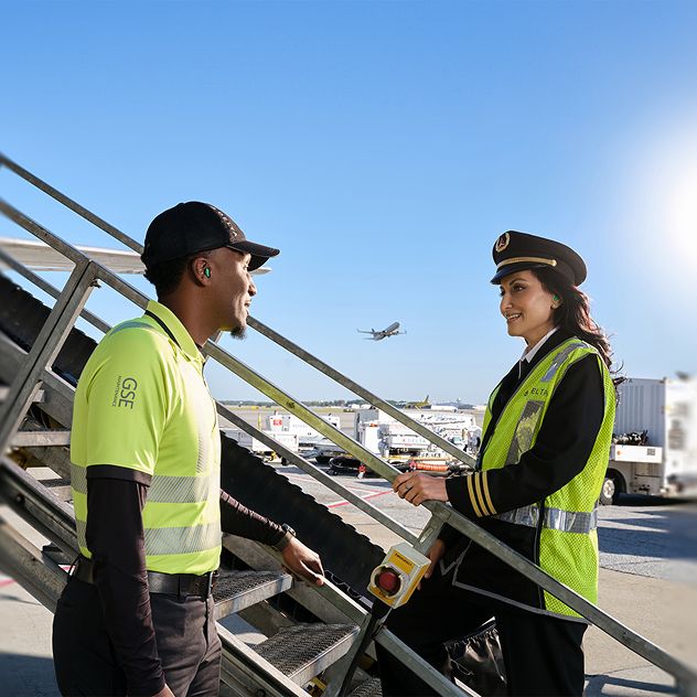 A female Delta pilot and mechanic talk near an aircraft boarding staircase.