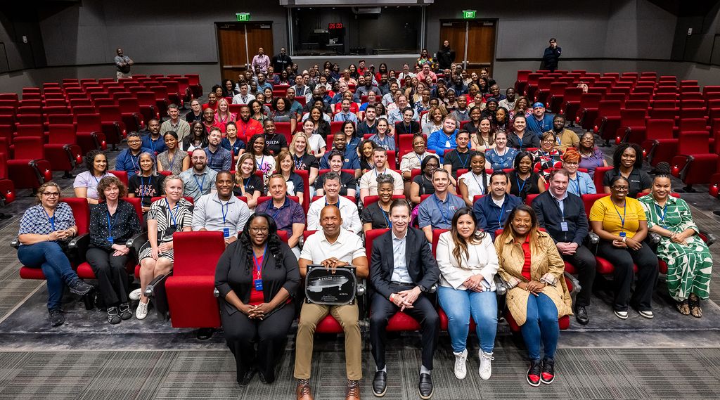 A large group of people are seated in an auditorium with red seats