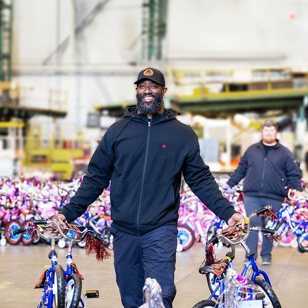 A Delta employee holding two children's bicycles in a large indoor space filled with colorful children's bicycles.