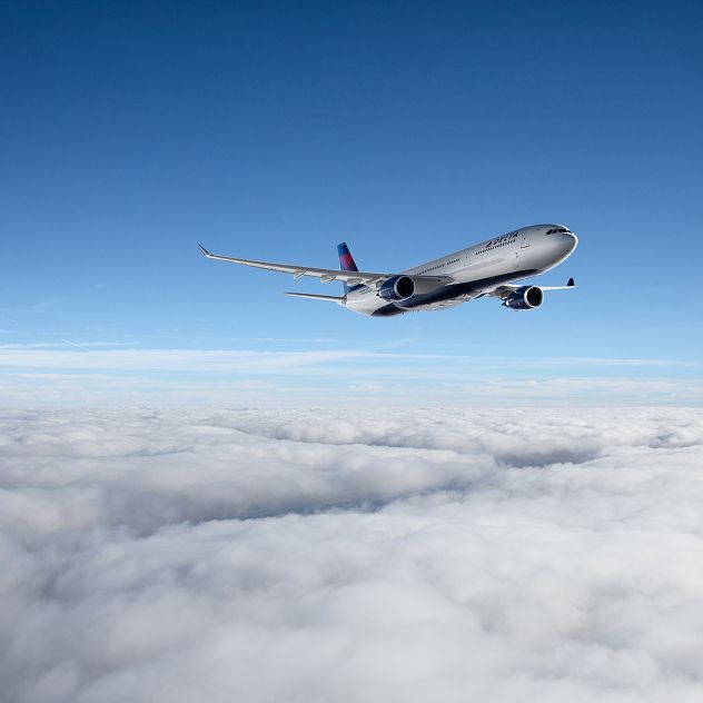 A Delta airplane is flying above a thick layer of clouds with a clear blue sky in the background.