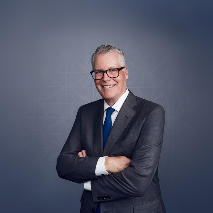 A professional portrait of a Delta Airlines CES wearing a dark suit, white shirt, and blue tie against a gray patterned background. To the left, text reads “Ed Bastian, Chief Executive Officer, Delta Air Lines,” with his stylized signature above the name.