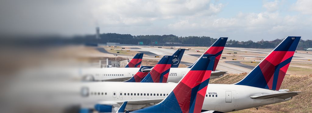 Multiple Delta aircraft lined up on the airport tarmac, showing tail sections with the red and blue Delta widget logo visible.