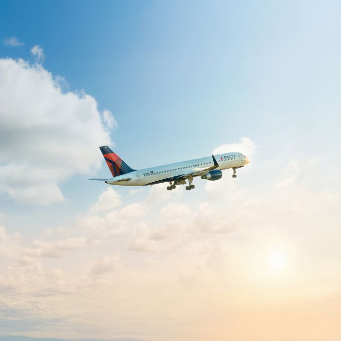 A Delta airplane viewed from the side, climbs through a partly cloudy sky