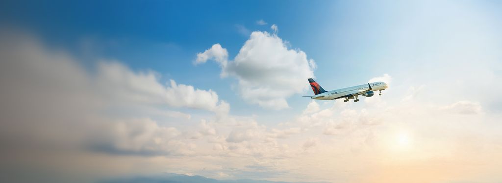 A Delta airplane viewed from the side, climbs through a partly cloudy sky
