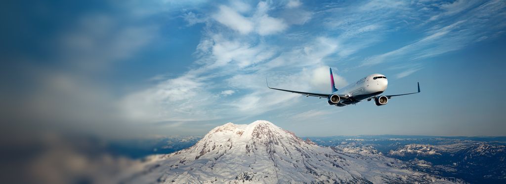 A Delta airplane flies above snow‑covered mountains under a clear blue sky.